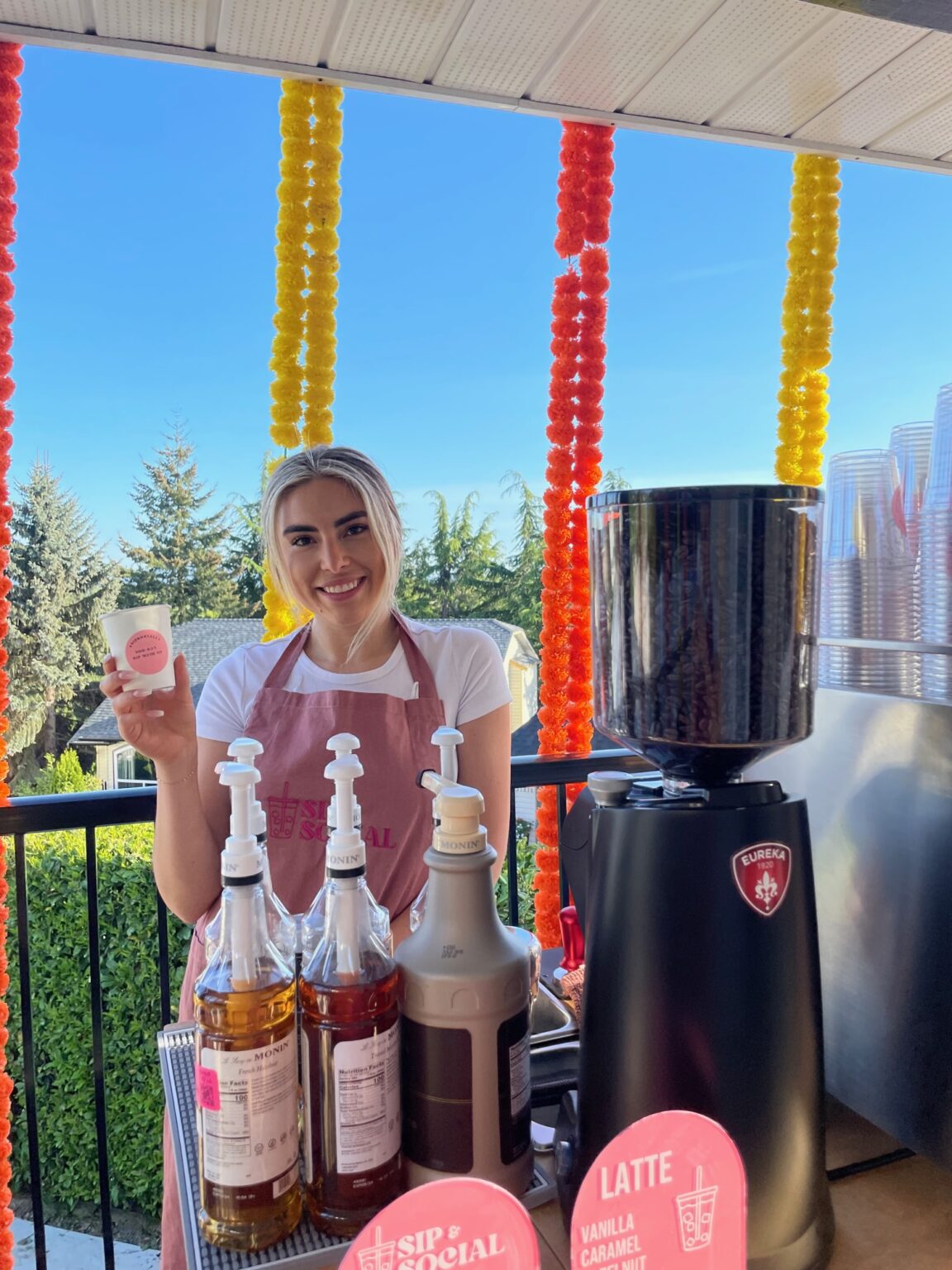 Sip & Social barista smiling into the camera behind the Sip & Social stand