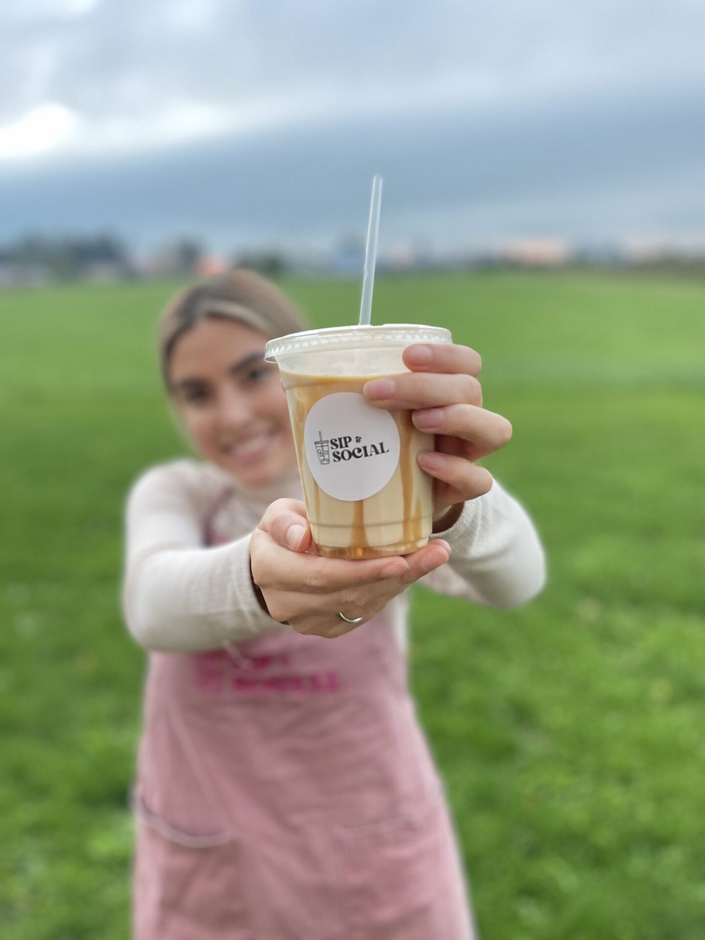 Founder of Sip & Social holding a coffee cup with a straw into the camera