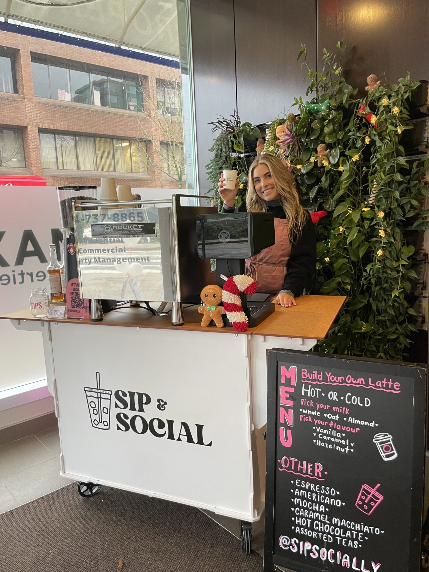 Sip & Social barista holding a cup into the camera behind their stand